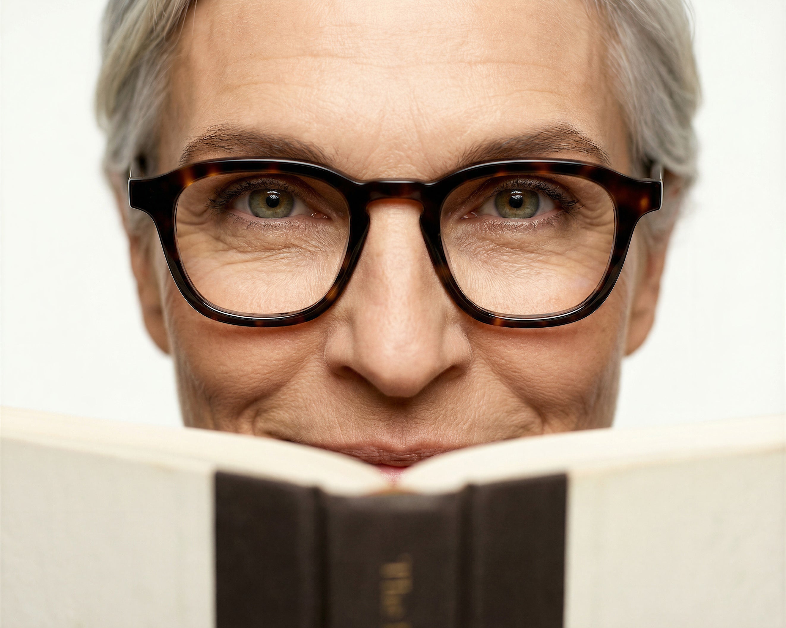 Close-up of a person with tortoiseshell glasses reading a book, against a simple white background.